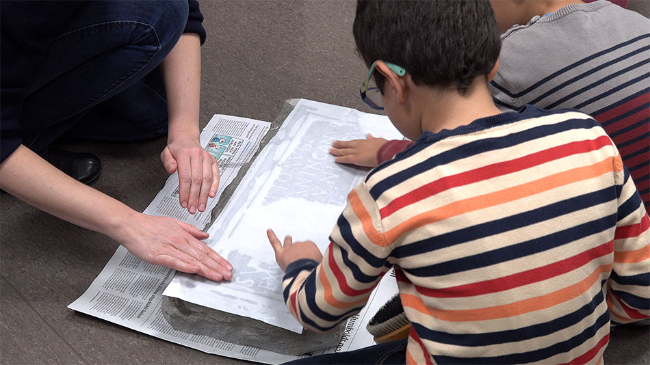 An experience for children and adults: A damp sheet of paper is laid on the stone in order to copy the inscription and produce what is called a “squeeze paper”.