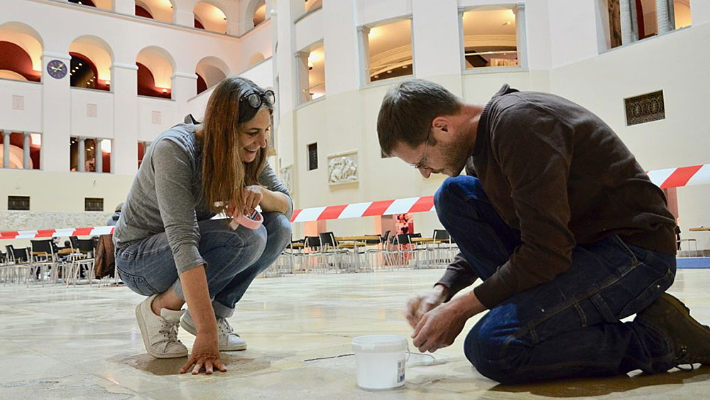 Artist Nadja Ullmann takes inspiration from the indentations and holes in the stone floor of the UZH Lichthof, which she has filled with inlays. Also pictured: Sven Mumenthaler (artist blacksmith).