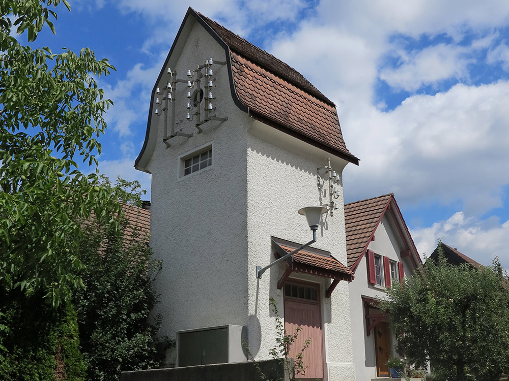 Dieses Türmchen in Weiach von 1910 ist eine der wenigen noch erhaltenen Transformatorenstationen im Bezirk Dielsdorf. Zu Beginn des 20. Jahrhunderts, als die Schweiz elektrifiziert wurde, hielt dieser neue Bautyp Einzug. Transformatorenstationen treten in unterschiedlichen Stilformen, zum Beispiel als historistische Backsteinbauten oder in den schlichten Formen des Reform- oder Heimatstils auf. Der Bau in Weiach zeigt ein geschwungenes Mansard-Giebeldach, das im Sinne des Heimatstils an vorindustrielle Bautraditionen anknüpft. (Bild: zVg)